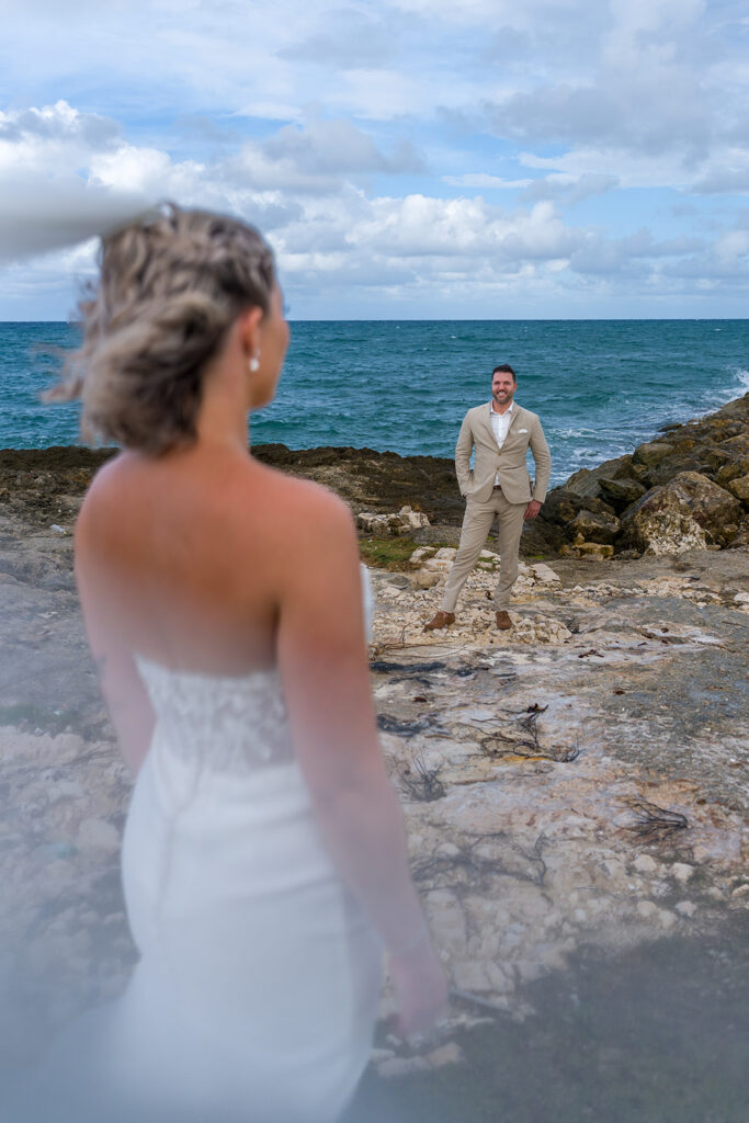 Mariée de dos regardant le marié sur des rochers en bord de mer, mariage à destination