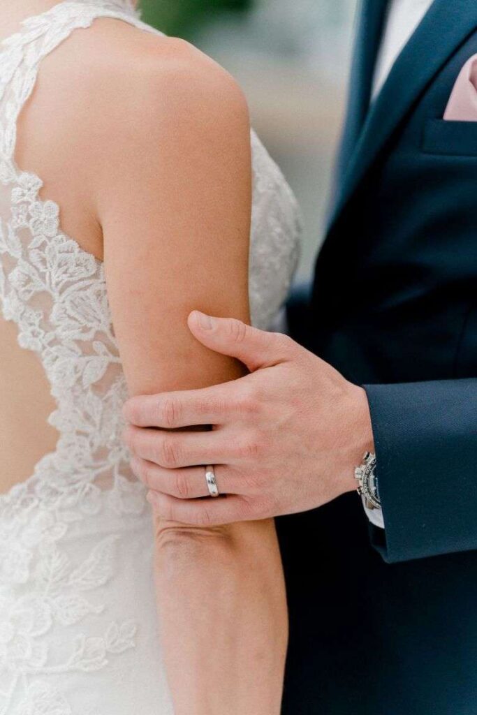 Gros plan de la main du marié sur le bras de la mariée, détail de mariage.