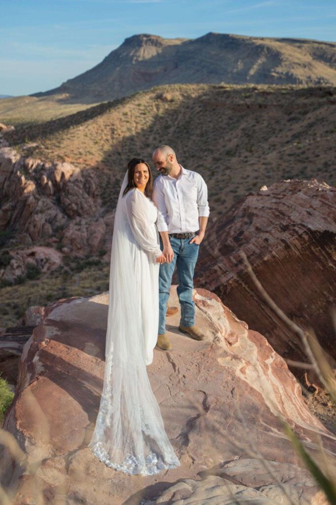 Mariés main dans la main devant un paysage désertique de montagnes, mariage à destination en pleine nature.