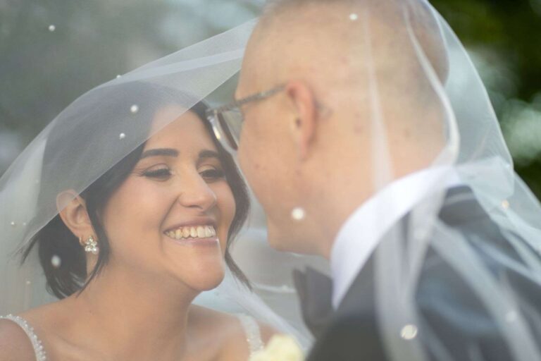 Mariés enlacés sous le voile de la mariée, moment intime et complice lors d'un mariage dans le Grand Montréal
