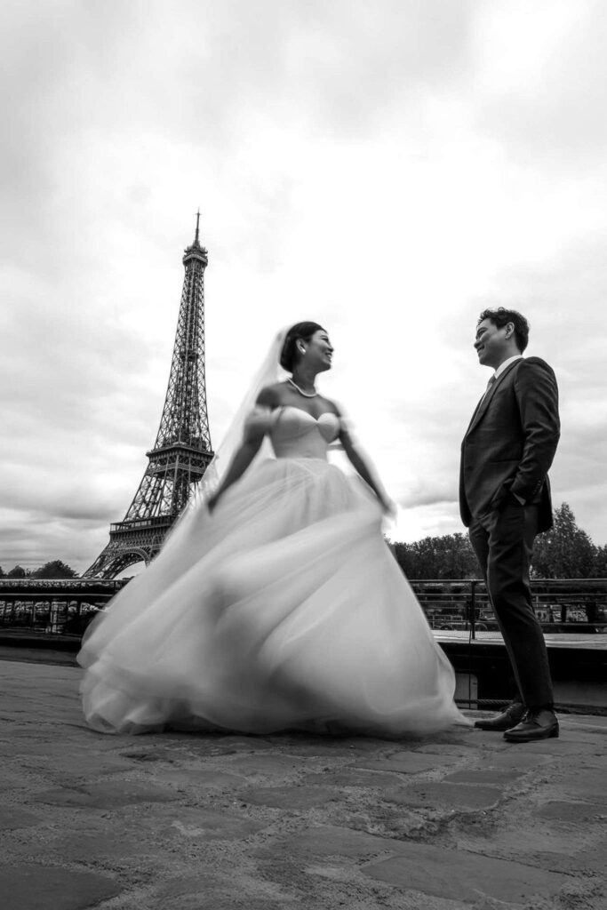 Mariés devant la tour Eiffel en robe blanche vaporeuse, photo de mariage noir et blanc à Paris.