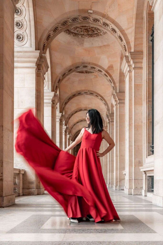 Mariée en robe rouge tourbillonnante sous une arcade parisienne, portrait éditorial de mariage à destination.