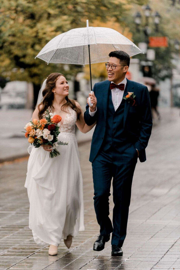 Mariés marchant sous un parapluie dans la rue, photo de mariage par jour de pluie.